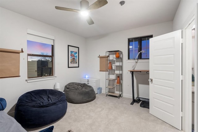 living area with baseboards, ceiling fan, and light carpet