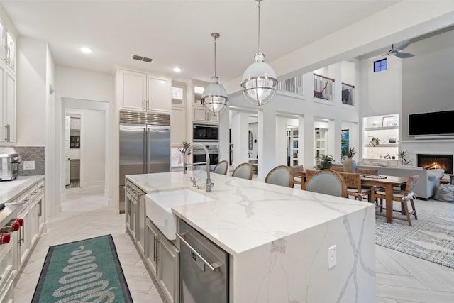 kitchen with a sink, visible vents, built in appliances, a kitchen island with sink, and a lit fireplace
