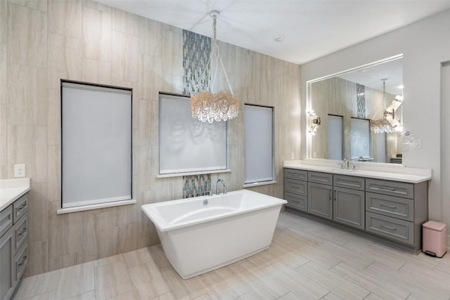 bathroom with vanity, a freestanding tub, a chandelier, and tile walls