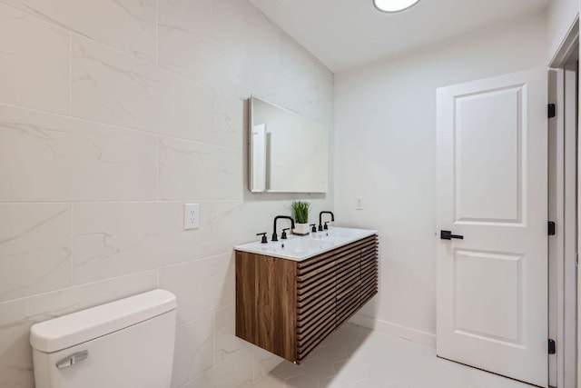 bathroom featuring double vanity, tile walls, a sink, and toilet