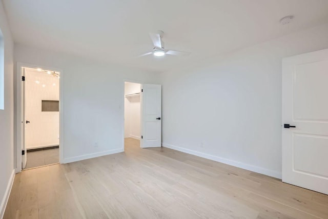 unfurnished bedroom with ensuite bathroom, baseboards, a ceiling fan, light wood-style floors, and a walk in closet