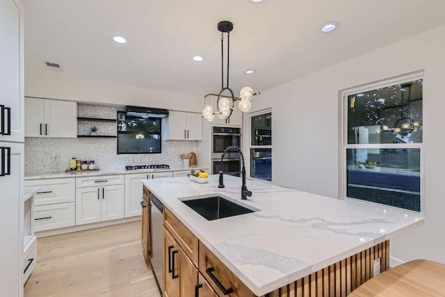 kitchen with white cabinetry, backsplash, stainless steel appliances, pendant lighting, and a sink