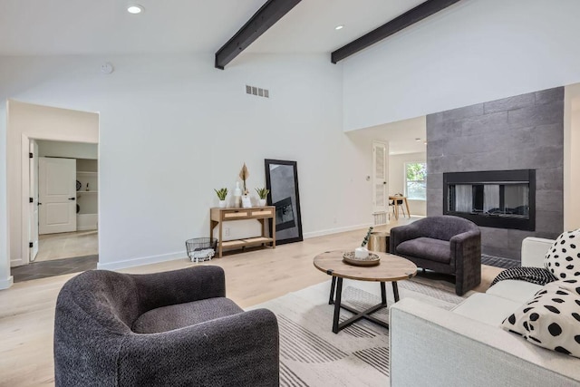 living room with visible vents, baseboards, a tiled fireplace, beamed ceiling, and light wood finished floors