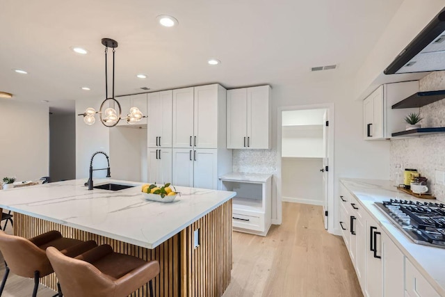 kitchen featuring visible vents, a sink, white cabinetry, light stone countertops, and stainless steel gas cooktop