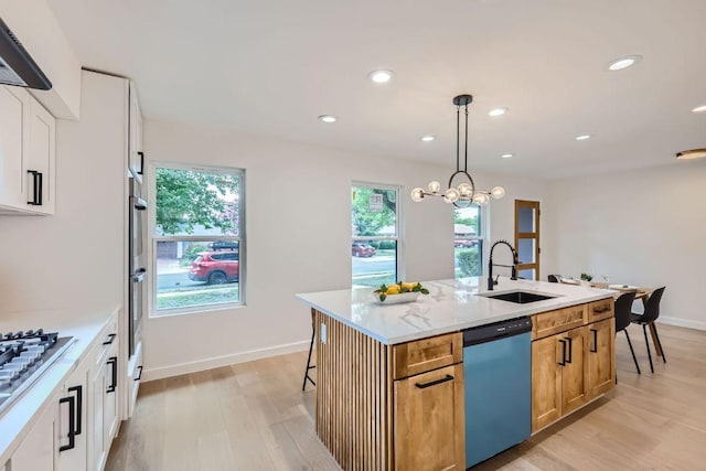 kitchen featuring light wood-style flooring, white cabinetry, appliances with stainless steel finishes, decorative light fixtures, and a center island with sink