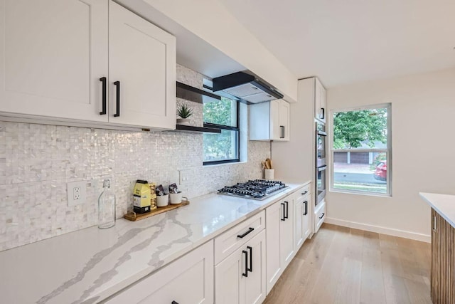 kitchen featuring light wood-style floors, light stone countertops, white cabinets, appliances with stainless steel finishes, and decorative backsplash