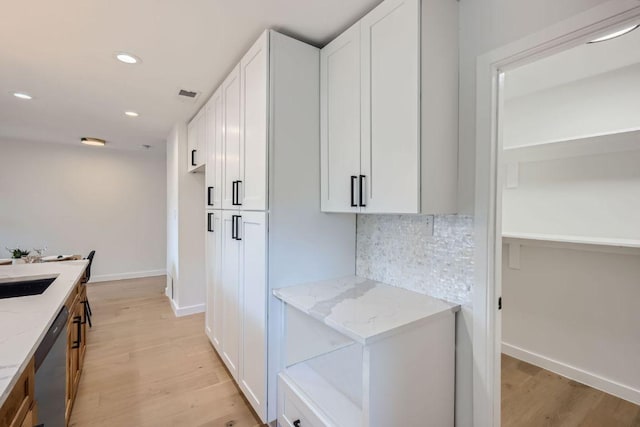 kitchen with tasteful backsplash, stainless steel dishwasher, white cabinetry, and light stone counters