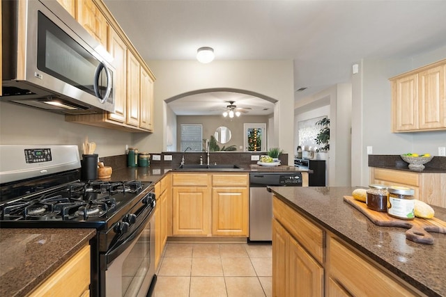 6220 Seville Dr, Austin, TX 78724 - kitchen featuring appliances with stainless steel finishes, light brown cabinetry, arched walkways, light tile patterned flooring, and dark stone countertops