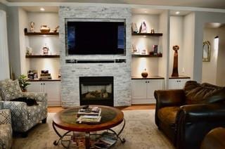 122 Camp Dr, Georgetown, TX 78633 - living room with a stone fireplace, wood finished floors, ornamental molding, and built in shelves