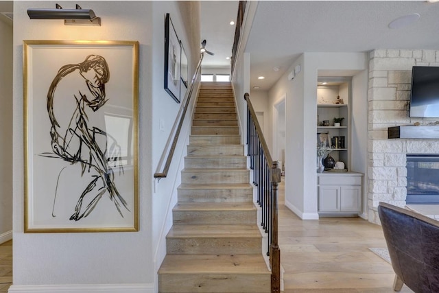 304 Ashburn Cv, Austin, TX 78738 - stairs featuring a stone fireplace, wood finished floors, baseboards, built in shelves, and recessed lighting