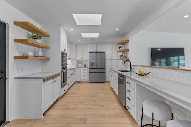 3306 Whiteway Dr, Austin, TX 78757 - kitchen with open shelves, a sink, a skylight, light wood-style floors, and appliances with stainless steel finishes