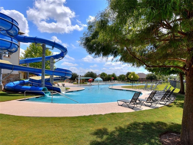 community pool featuring fence, a patio area, a water slide, and a yard