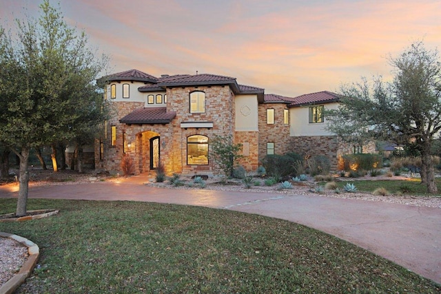 mediterranean / spanish-style house featuring stucco siding, a yard, and stone siding