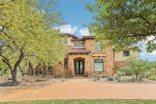 mediterranean / spanish home featuring french doors, stucco siding, a tile roof, and stone siding
