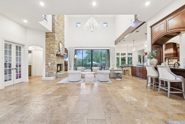 living room featuring recessed lighting, stone tile flooring, a notable chandelier, a towering ceiling, and french doors