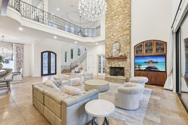 living area featuring stairway, a chandelier, a stone fireplace, a towering ceiling, and french doors
