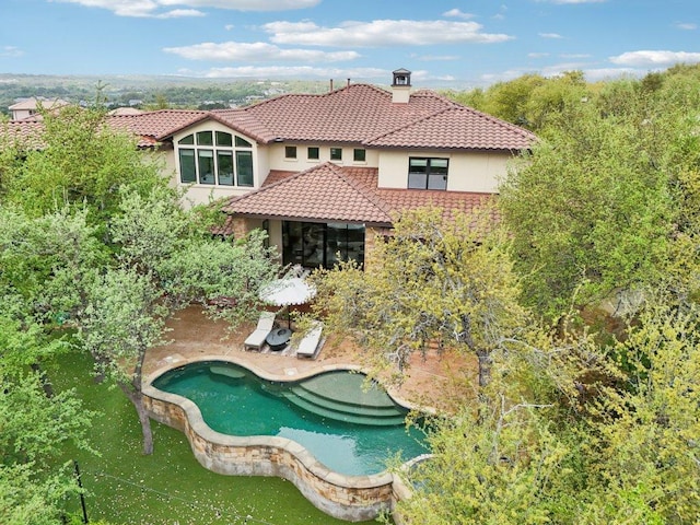 back of property featuring a tile roof, a patio, an outdoor pool, a chimney, and stucco siding