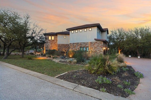 view of front of house with a front yard, stone siding, and stucco siding