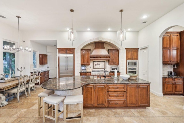 kitchen with built in appliances, custom exhaust hood, tasteful backsplash, and stone tile flooring