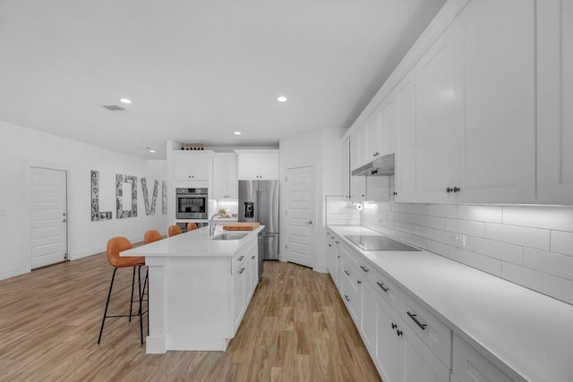 16512 Fetching Ave, Manor, TX 78653 - kitchen featuring under cabinet range hood, stainless steel fridge, a sink, light wood-style flooring, and a breakfast bar