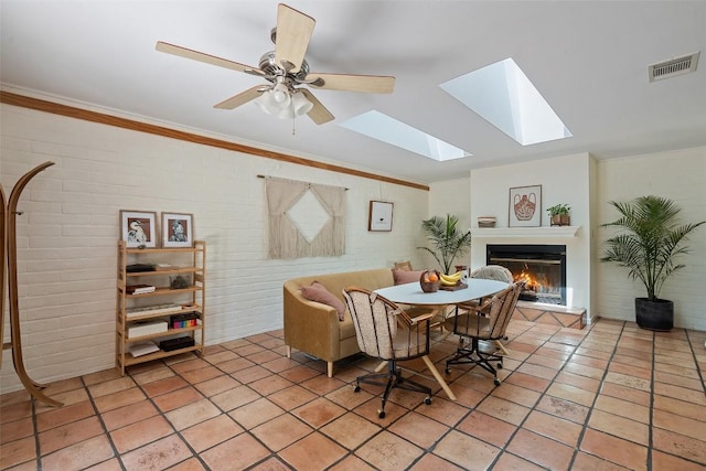 1005 Lisa Dr, Austin, TX 78733 - dining area with a lit fireplace, crown molding, brick wall, a skylight, and light tile patterned floors