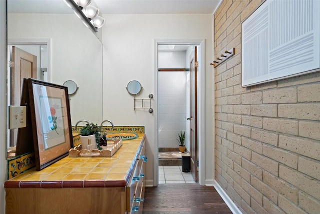 1005 Lisa Dr, Austin, TX 78733 - bathroom featuring wood finished floors, vanity, brick wall, and a shower