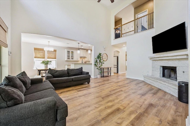 12907 Gordons Hvn, San Antonio, TX 78253 - living area with light wood-style flooring, a towering ceiling, a stone fireplace, ceiling fan, and arched walkways