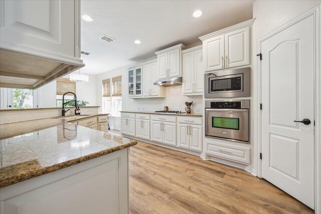 12907 Gordons Hvn, San Antonio, TX 78253 - kitchen featuring stainless steel appliances, under cabinet range hood, white cabinets, light wood-style floors, and light stone counters