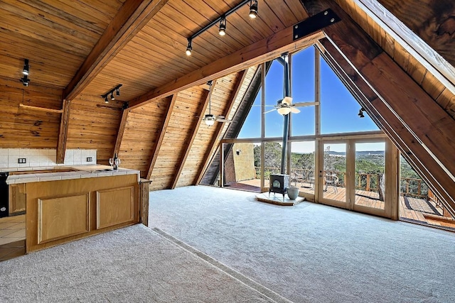 unfurnished living room featuring rail lighting, carpet flooring, wooden walls, a wood stove, and wood ceiling