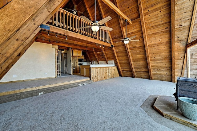 unfurnished living room featuring lofted ceiling with beams, a wood stove, ceiling fan, carpet, and wood ceiling