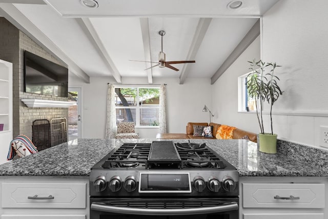8604 Primrose Ln, Austin, TX 78757 - kitchen featuring gas stove, a ceiling fan, dark stone counters, white cabinetry, and a brick fireplace