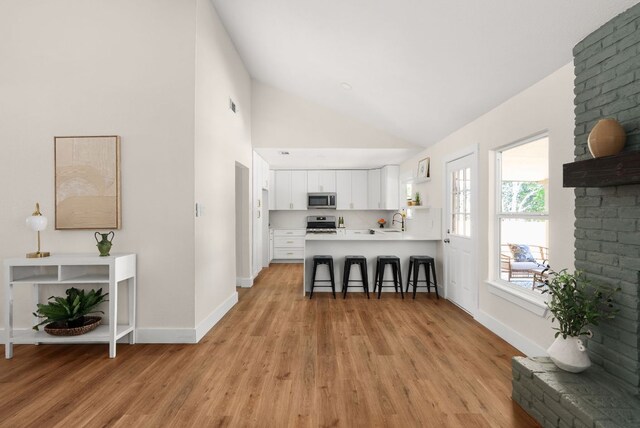 9005 Quail Creek Dr, Austin, TX 78758 - kitchen with stainless steel appliances, a breakfast bar, light wood-style floors, white cabinets, and high vaulted ceiling