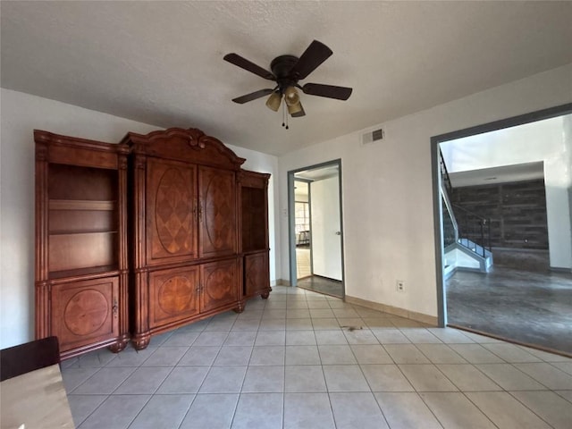 interior space featuring baseboards, light tile patterned floors, stairs, visible vents, and ceiling fan