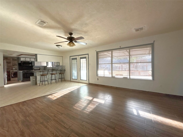 unfurnished living room with light wood-type flooring, ceiling fan, visible vents, and a textured ceiling