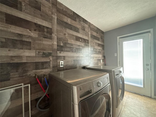 laundry area featuring laundry area, wooden walls, a textured ceiling, and washer and clothes dryer