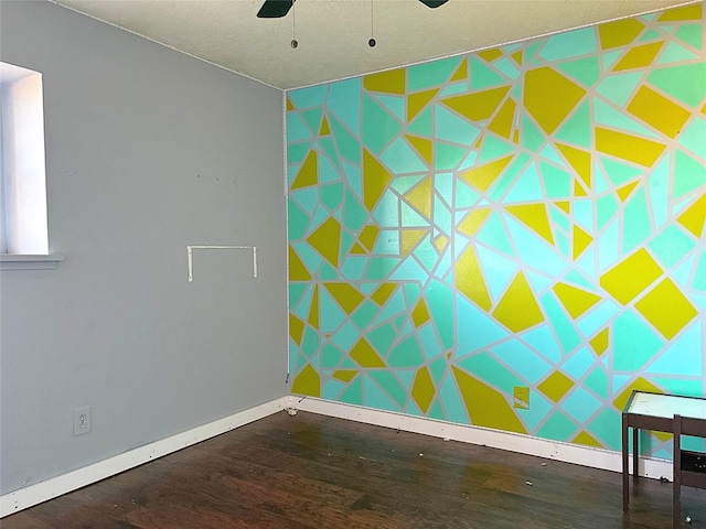 spare room with an accent wall, baseboards, wood finished floors, and ceiling fan