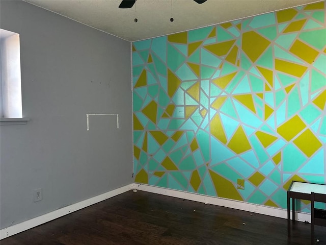 unfurnished room with baseboards, a ceiling fan, an accent wall, and wood finished floors