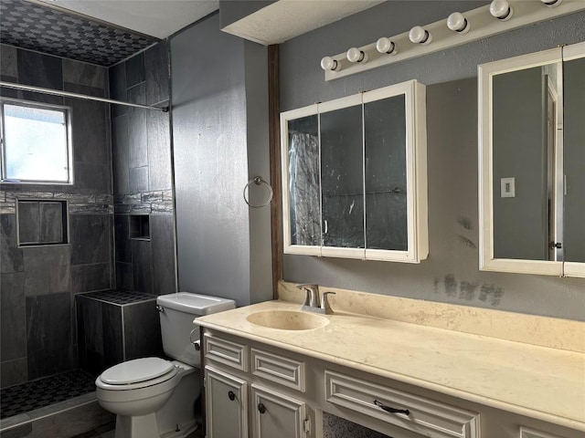 full bath with vanity, a tile shower, and toilet