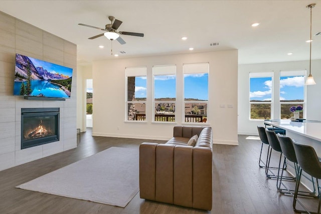 living room featuring a ceiling fan, visible vents, a tile fireplace, recessed lighting, and dark wood-type flooring