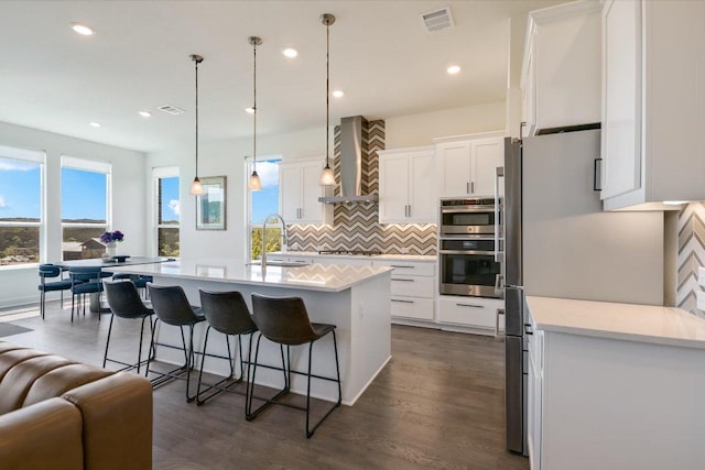 kitchen with wall chimney range hood, backsplash, visible vents, a sink, and white cabinets