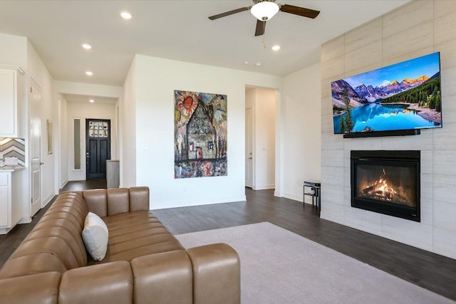 living area featuring a tiled fireplace, a ceiling fan, baseboards, recessed lighting, and dark wood-type flooring