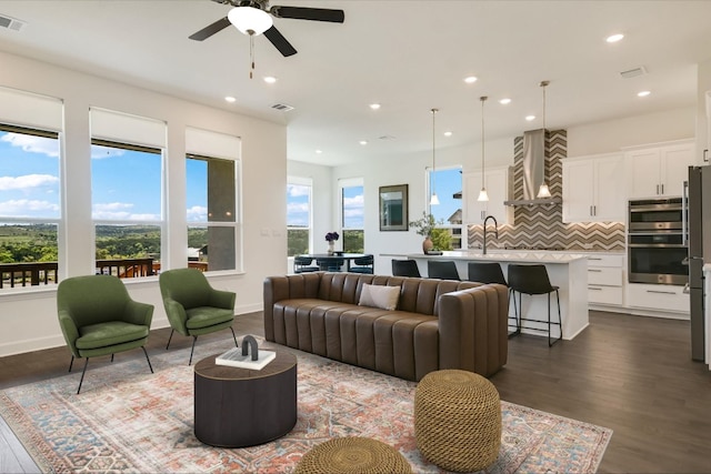 living room featuring plenty of natural light, a ceiling fan, dark wood-style flooring, and visible vents
