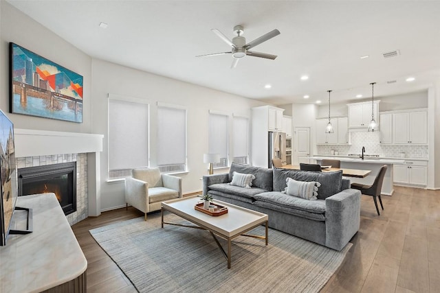 living room with recessed lighting, a ceiling fan, a glass covered fireplace, and light wood-type flooring
