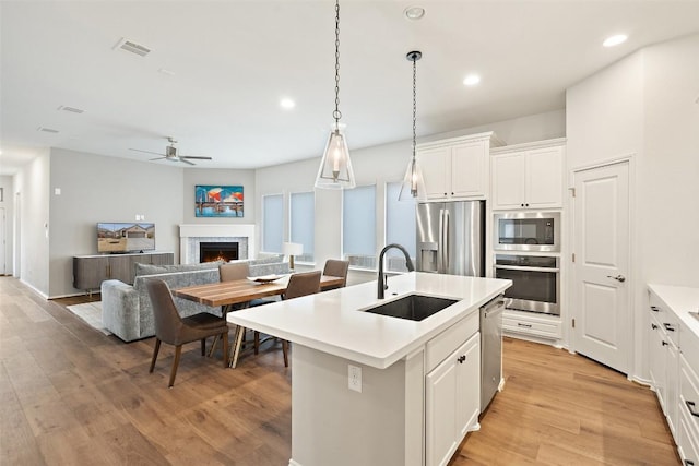 kitchen featuring a ceiling fan, a sink, light wood-style floors, a lit fireplace, and appliances with stainless steel finishes