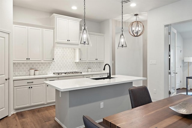 kitchen featuring stainless steel gas stovetop, dark wood finished floors, backsplash, light countertops, and a sink