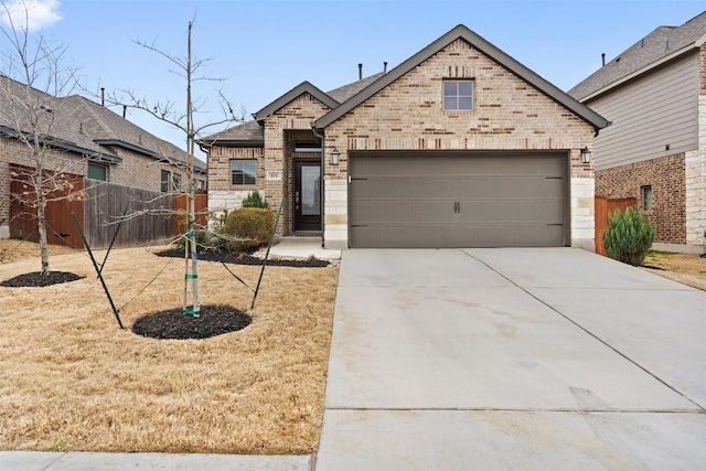 french country style house featuring brick siding, an attached garage, concrete driveway, and fence