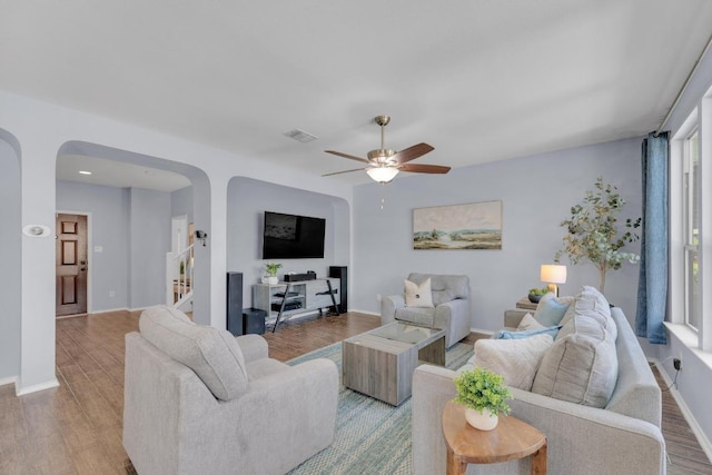 living room with baseboards, stairway, a ceiling fan, arched walkways, and wood finished floors