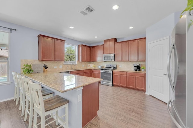 5812 Pescia St, Round Rock, TX 78665 - kitchen with appliances with stainless steel finishes, a peninsula, a sink, light wood-type flooring, and a kitchen breakfast bar