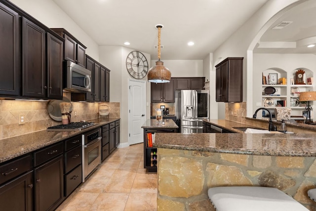 215 Choke Canyon Ln, Georgetown, TX 78628 - kitchen with appliances with stainless steel finishes, arched walkways, dark stone countertops, dark brown cabinets, and recessed lighting
