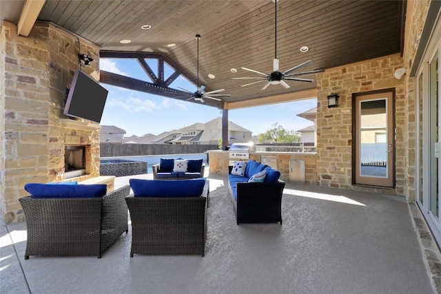 view of patio / terrace with an outdoor kitchen, ceiling fan, an outdoor living space with a fireplace, a grill, and fence